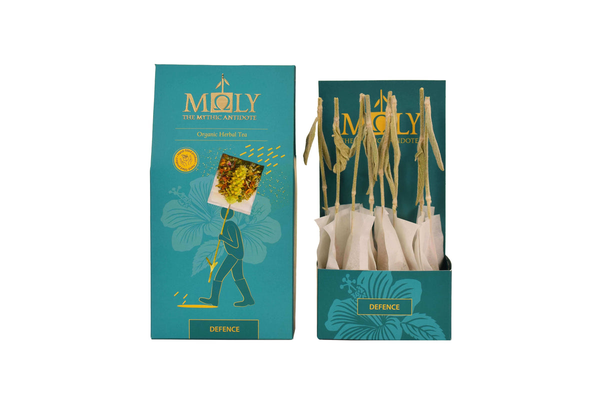 Eine türkisblaue Verpackung des MΟLY Defence BIO mit goldener Schrift sowie aufgedruckten Pflanzen. Zentral ist ein Bild aufgedruckt, welches einen Teebeutel mit Inhalt zeigt aus dem der Stengel der Sideritis scardica (griechischer Bergtee) herausragt. Daneben ist der Inhalt zu sehen, der aus zehn einzelnen Teebeuteln mit jeweils einem Sideritis-Stengel besteht.
